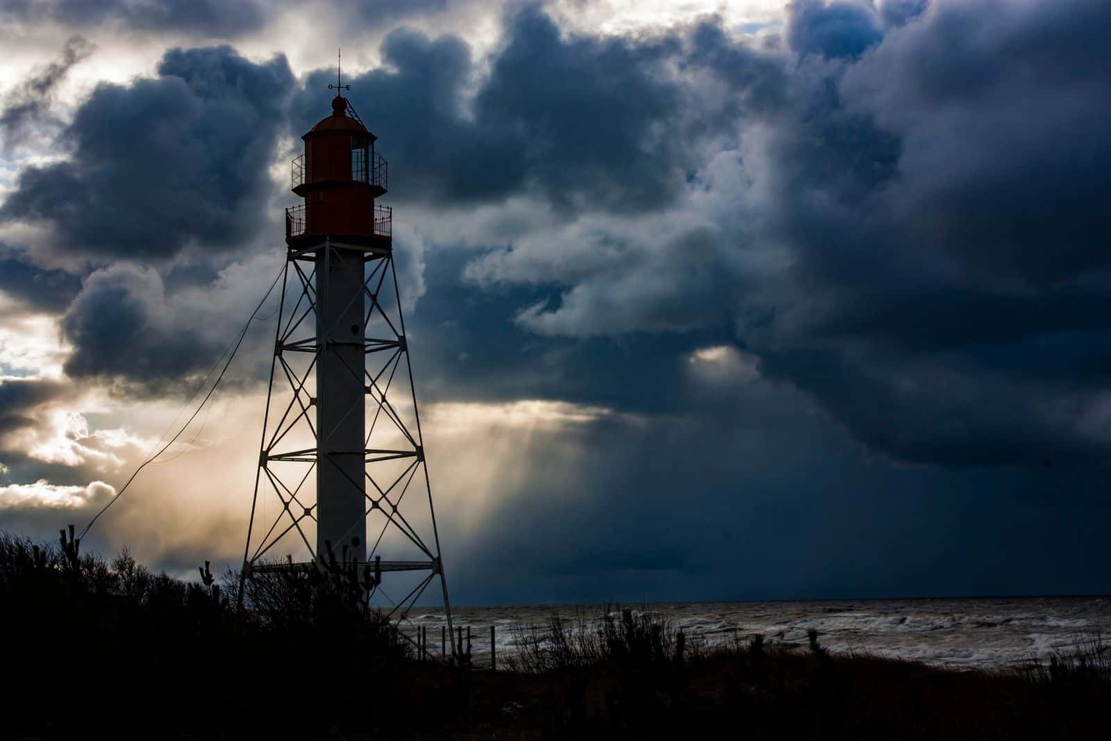 Lighthouse on a stormy coast with dark clouds and sunlight breaking through.