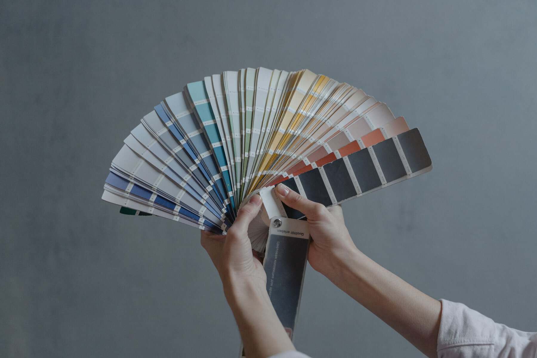 Hands holding a fan of paint colour swatches against a grey background